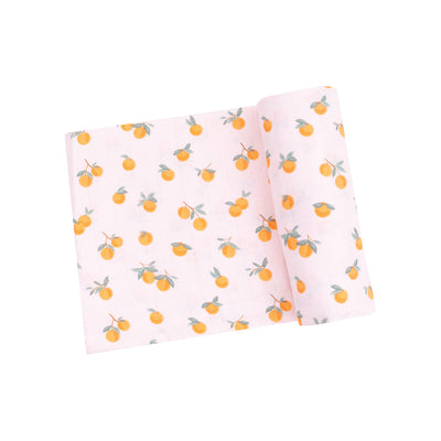 The Sweet Clementine Muslin Swaddle Blanket by Angel Dear, crafted from organic cotton muslin, showcases an orange fruit design with green leaves on a light pink background—ideal for swaddles or as a charming baby gift.