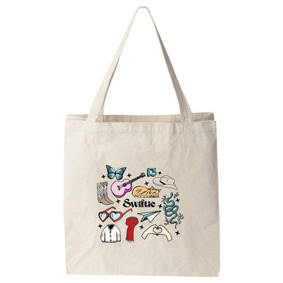 The Swiftie Collage Colorful Tote Bag by Moonlight Makers is a beige cotton tote printed in Asheville, NC with non-toxic ink. It features illustrations of a butterfly, guitar, snake, cowboy boot, hat, heart glasses, red lipstick & Swiftie text.