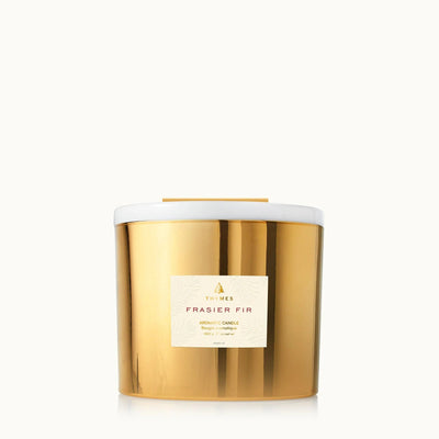 The Thymes Frasier Gold Poured 3-Wick Candle features a gold metallic jar with a white lid, offering a signature mountain fresh scent, shown against a plain white background.