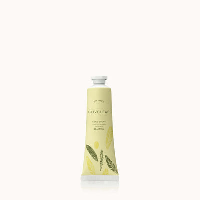 The Olive Leaf Petite Hand Creme by Thymes comes in a 30 ml (1 fl oz) tube with leaf illustrations on a pale green design, enriched with shea butter. The product stands upright against a plain white background.