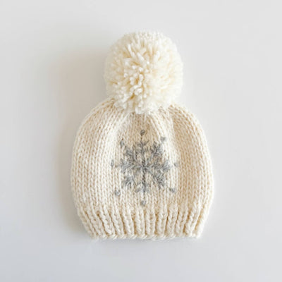 Knitted white beanie with a pom-pom and snowflake design on a light gray background