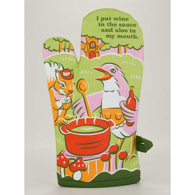 The Blue Q Wine In My Mouth Oven Mitt features a colorful cartoon bird with a wine bottle, a squirrel by the pot, and charming forest and mushroom details. The mitt reads: I put wine in the sauce and also in my mouth.