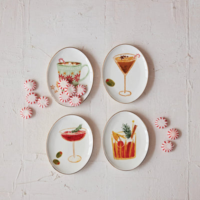 The Holiday Cocktail Stoneware Dishes by Creative Co-op feature four oval plates, each with a unique festive cocktail illustration and a green olive. Arranged on a white textured surface, they're surrounded by red and white peppermint candies.