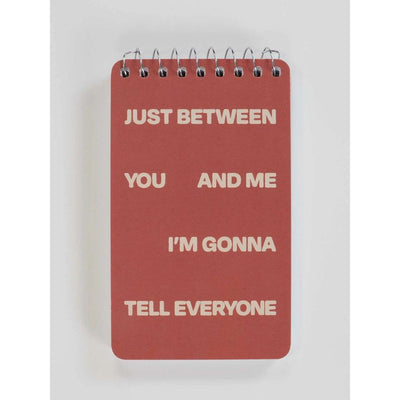 The Blue Q Between Me and You Spiral Notebook is a red, funny pocket notebook with cream-colored text that reads: JUST BETWEEN YOU AND ME IM GONNA TELL EVERYONE.