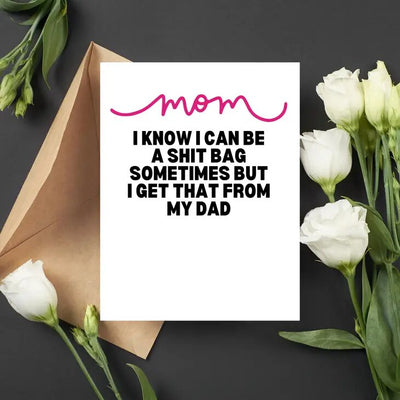 The I Get It from Dad Mothers Day Greeting Card by As Told by Ellie features a 4.25in x 5.5in A2 card against a black background with white roses. The card reads Mom, I know I can be a shit bag sometimes but I get that from my dad, with mom in pink script, and includes an open brown envelope and blank interior.